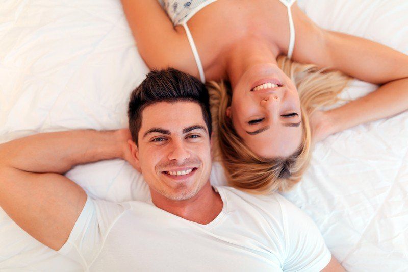 A man and a woman are laying on a bed with their heads together and smiling.